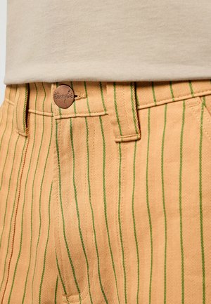 Vaaleanruskeat raidalliset housut, joissa on pystysuorat vihreät viivat, vyötäröllä ruskea nappi, tarkkaa ommelta ja kalanruotokuvio.