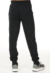 Zwarte sweatpants met een elastische tailleband, zijzakken en een tapered fit; gecombineerd met grijze en zwarte sneakers. Glad katoenen textuur.