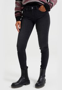 Jeans skinny negros con una cintura alta, diseño de cinco bolsillos y tela de mezclilla elástica, combinados con botas tobilleras negras de suela gruesa.