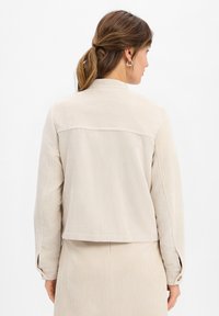 Beige Cordjacke mit leicht verkürztem Schnitt, ausgestattet mit einer glatten Textur und einem Rückenpasse-Detail, kombiniert mit passendem beige Stoff.