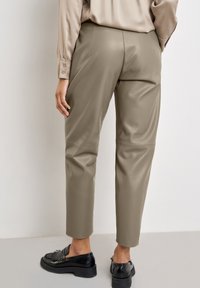 Figurformade, högmidjade olivgröna byxor i konstläder med en slät yta och synliga sömdetaljer, kombinerat med svarta loafers.