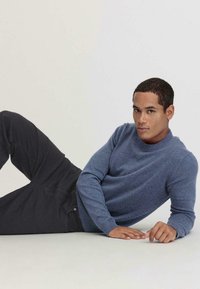 Blauer Strickpullover mit rundem Ausschnitt, kombiniert mit dunklen Hosen. Der Stoff wirkt weich, mit gerippten Akzenten an den Ärmeln und dem Saum.