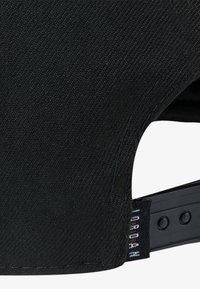 Berretto nero in tessuto testurizzato, con visiera curva e cinturino regolabile in plastica con etichetta logo sul lato.