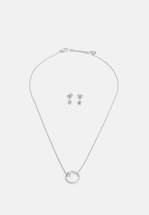 Collana d'argento con una catena sottile e un pendente circolare caratterizzato da una piccola pietra, abbinata a orecchini a clip a forma di fiore.