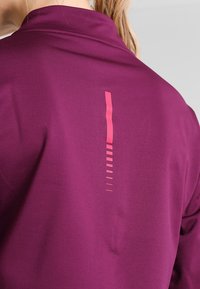 Lila träningsskjorta med en slät textur och en vertikal rosa grafisk design på baksidan, med olika tunna horisontella linjer.