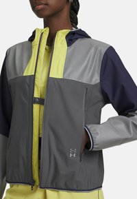 Gray and navy jacket with yellow accents, featuring a zip closure, hood, and side pockets. Made from lightweight, textured material.