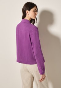 Lila strukturierte Bluse mit langen Ärmeln, Knopfmanschetten und einem Kragen. Der Rücken weist eine Nahtdetail auf und hat einen lockeren Schnitt.