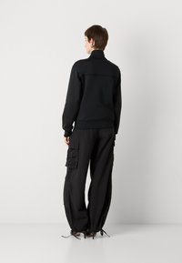 Black sweatshirt with a high collar, paired with black cargo pants featuring multiple pockets and drawstring hems. Smooth fabric texture.