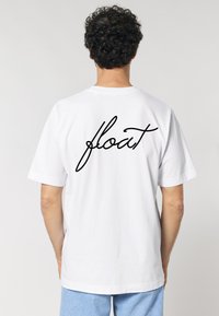 Tricou alb din bumbac, cu mâneci scurte și gât rotund, având cuvântul "float" scris cu litere cursive negre pe spate.
