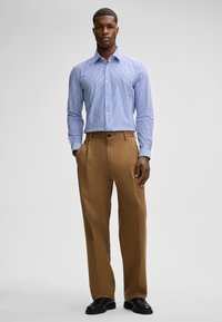 Camicia a righe blu chiaro con colletto button-down, abbinata a pantaloni beige con pieghe e scarpe nere, caratterizzata da un design classico.