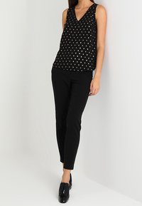 Haut noir sans manches avec un col en V et un motif à pois métalliques, associé à un pantalon noir ajusté et des mocassins noirs brillants.