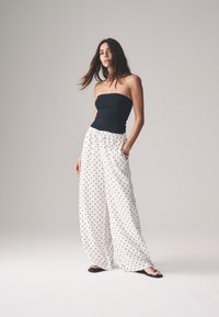 Črni brezrokavnik v kombinaciji z ohlapnimi belimi hlačami z belimi pikami. Mehak material, široke noge in žepi, dopolnjeno s črnimi sandali.