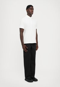 Hvit kortermet polo-skjorte med krage, sammen med svarte bukser med sidelommer og svarte joggesko. Enkel og funksjonell design.