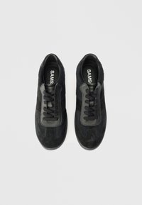 Mustad mustad ja nahast mustad tossud, millel on ümmargune nina, lame mustad paelad ja tekstureeritud külgpaneelid. Brändinimi on nähtav sees.