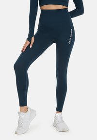 Tmavě modré legíny s vysokým pasem a ribovanou texturou s logem "SQUATPROOF". V kombinaci s bílými sportovními botami.