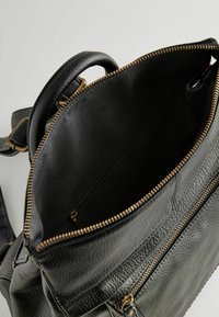 Sac en cuir noir avec une poignée supérieure unique, une fermeture éclair dorée et un intérieur spacieux comprenant une poche zippée supplémentaire.