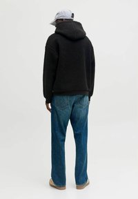 Schwarzer Fleece-Hoodie mit hohem Kragen, oversized Design und Kängurutasche, kombiniert mit blauen Jeans und beigen Schuhen.