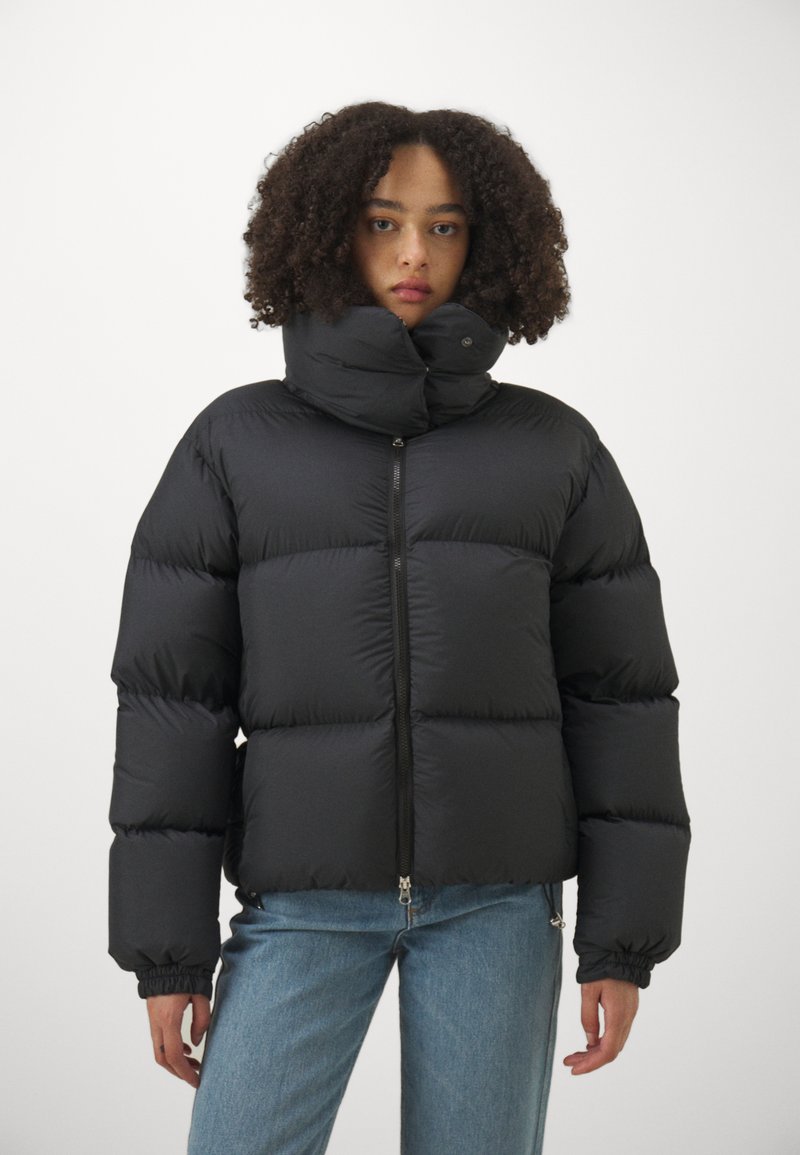 Fekete puffarongy sima, fényes anyagból, magas gallérral és cipzáros záródással. Rugalmas mandzsettákkal és dobozos formával rendelkezik a melegség érdekében.