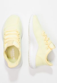 Ljust gula träningsskor med en mesh-överdels, vadderad krage och en vit gummisula med texturerade mönster och elastiska snören.