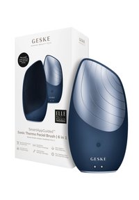 Brosse faciale sonique bleue avec une surface en silicone texturé et un sommet lisse, emballée dans une boîte blanche comportant les détails du produit et les logos.