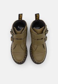 Botines de piel verde oliva con dos tiras de Velcro, forro negro y costuras amarillas a lo largo de la suela de goma negra. Diseño de puntera redonda.