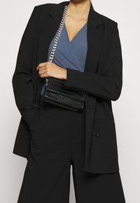 Černá kabelka z umělé kůže s texturou krokodýlí kůže, stříbrný řetízek na nošení, obdelníkový tvar a magnetické zapínání. Nositelná s modrým topem a černým sako.