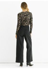 Long-sleeve animal print top in beige and black, paired with high-waisted black wide-leg jeans and sleek black ankle boots.