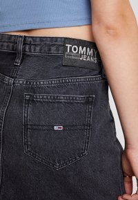 Gonna in denim nero con vita aderente e tasca sul retro. Presenta un'etichetta Tommy Jeans testurizzata e un piccolo logo ricamato sulla tasca.