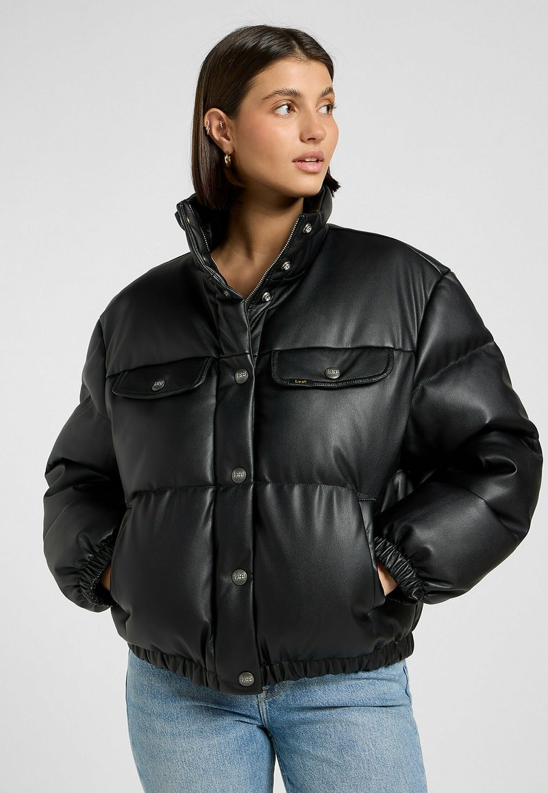 Chaqueta acolchada negra en cuero sintético con un alto cuello, botones a presión y dos bolsillos frontales. Presenta puños y dobladillo elásticos para un ajuste ceñido.