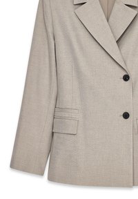 Helles beige Blazer mit zwei schwarzen Knöpfen, abgesetztem Reverskragen und einer Klapptasche auf der linken Seite.
