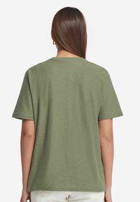 Olivgrön t-shirt med kort ärm och rund halsringning, avslappnad passform och en texturerad tygkvalitet. Bakre vy visar en slät, sömlös design.