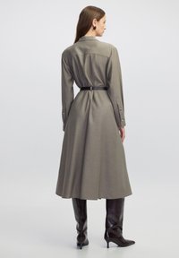 Lang, lichtgrijze jurk met een ceintuur in de taille, knoopmanchetten en een vloeiende rok. Draag met strakke, glanzende, donkerbruine enkellaarzen tot aan de knie.