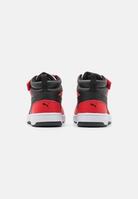 Baskets montantes noires et rouges avec un col rembourré, une sangle Velcro, une semelle blanche et un accent de logo distinctif sur le talon.