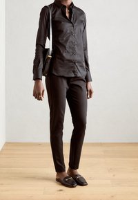 Camicia nera con bottoni e maniche lunghe, abbinata a pantaloni neri aderenti e mocassini senza lacci con dettagli dorati.
