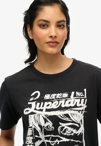 T-shirt in cotone nero con una stampa grafica bianca che presenta un volto illustrato e il testo "Superdry" in evidenza.