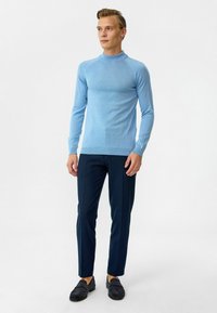 Lichtblauwe gebreide trui, met geribbelde hals en manchetten, gecombineerd met navy slim-fit broek en donkere loafers, met een gladde textuur overal.
