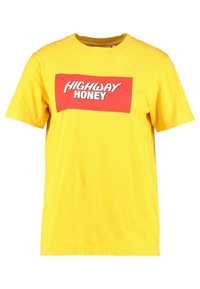Žluté bavlněné tričko s krátkým rukávem a kulatým výstřihem, na přední straně má červený obdélníkový grafický motiv s textem "HIGHWAY HONEY" v bílé barvě.