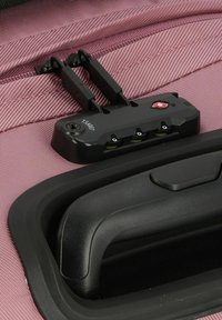 Svart kombinationslås med tre hjul, monterat på en rosa tygyta. Handtaget är ergonomiskt utformat med en slät yta.