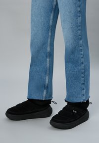 Scarpe slip-on nere imbottite con una tomaia testurizzata, abbinate a jeans a gamba dritta blu chiaro con una cucitura verticale a contrasto.