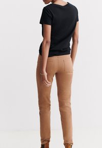 Camiseta negra de algodón combinada con jeans ceñidos color beige. La camiseta tiene un escote redondeado; los jeans cuentan con bolsillos traseros y una textura suave.