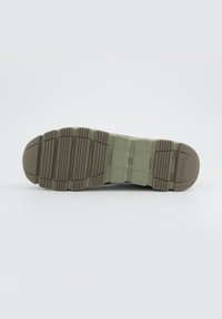 Rubber sneaker sole in beige and olive green with textured treads, featuring a patterned design for grip and a smooth toe cap.
