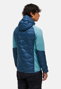 Gewatteerde jas met een capuchon, gemaakt van een donkerblauw, glanzend materiaal met golfpatronen. Lichtblauwe secties op de mouwen en zijkanten.