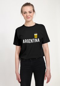 Černé tričko s nápisem "ARGENTINA" velkými bílými písmeny, zdobené logem a dvěma zlatými hvězdami nahoře.