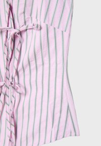 Tissu rose avec des rayures verticales vertes et blanches, orné de nœuds noués le long d'une couture.