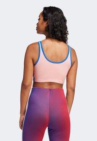 Růžová sportovní podprsenka s modrými akcenty, s krátkým designem a úzkými ramínky, doplněná legínami vysokého pasu s gradientem od červené po fialovou.