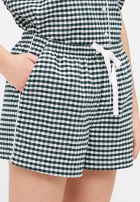 Grønne og hvite rutete shorts med elastisk midjebånd, snor, og sidelommer; laget av et mykt, lett stoff.