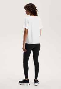 Hvid kortærmet t-shirt parret med sorte leggings og sorte træningssko. T-shirten har et simpelt, lige design med en rund halsudskæring.