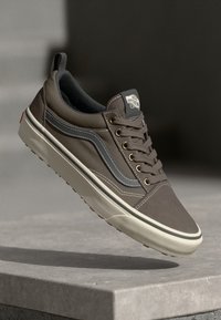 Brown canvas sneaker with gray accents, white stitching, and a rubber sole. Features round laces and a logo patch on the tongue.