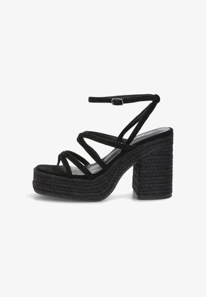 Sandalia negra de tacón alto con suela plataforma trenzada, múltiples tiras finas cruzando el pie y correa ajustable en el tobillo con hebilla.