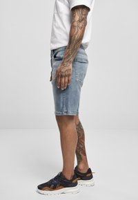 Lys blå denimshorts har en lige pasform, en slidset kant og baglommer. Bæret med sorte sneakers med orange detaljer og en hvid skjorte.